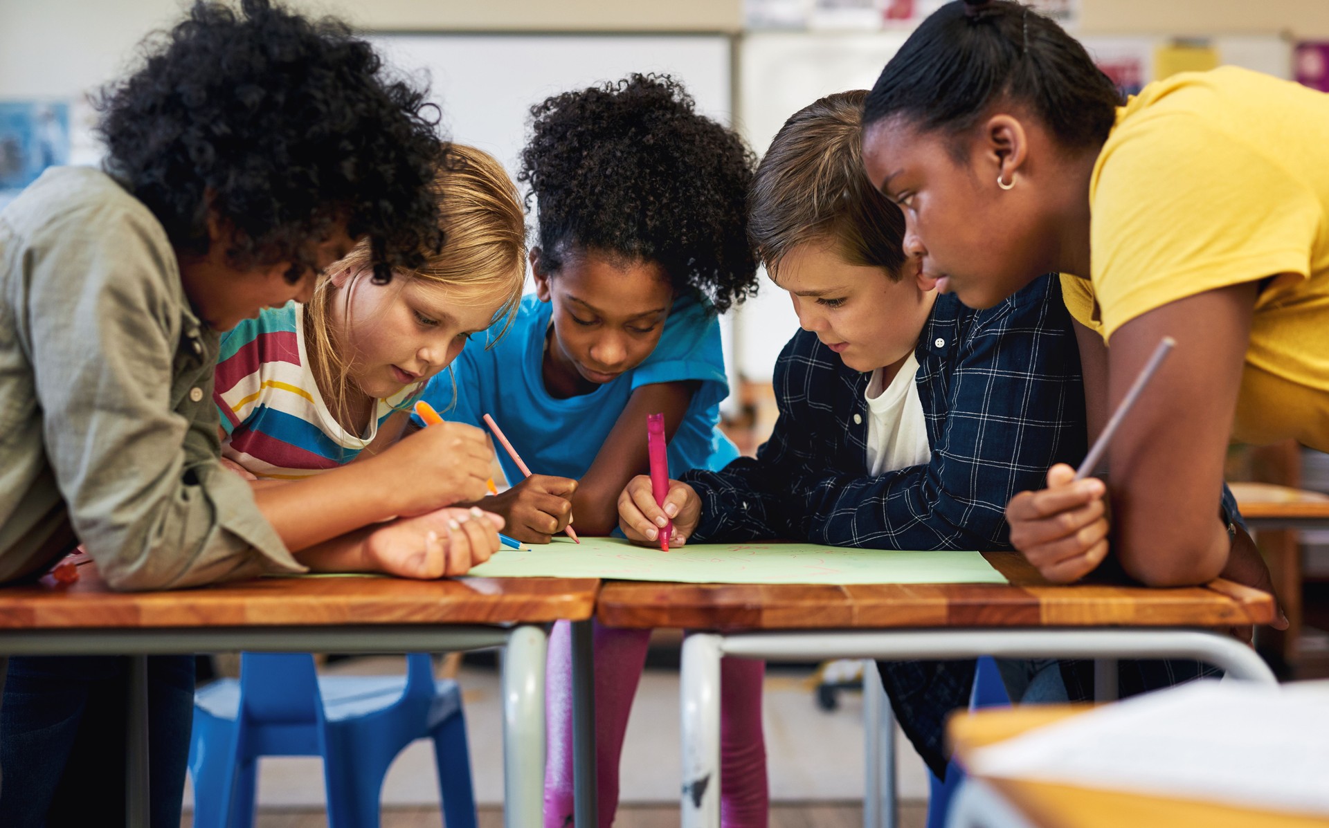Shot of a diverse group of children huddled together and colouring in their classroom at school